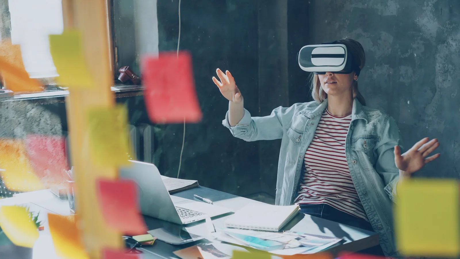 노트북과 메모가 놓인 책상에서 VR 헤드셋을 사용하는 사람