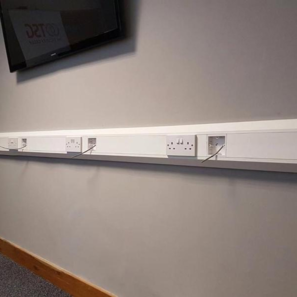 Dado trunking fixed to an office wall with power sockets and network ports for flexible connectivity.