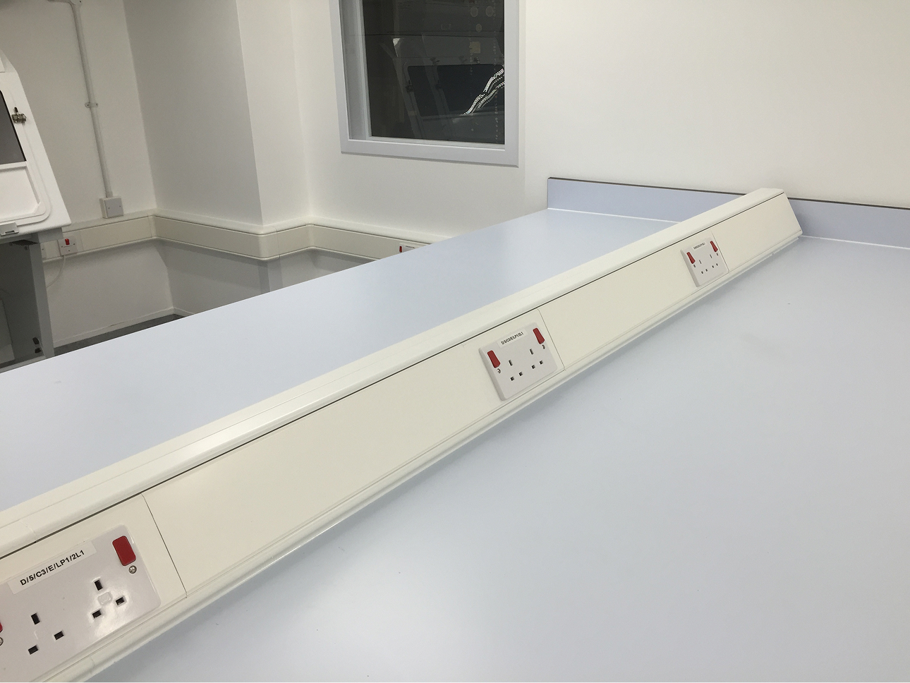 Corner dado trunking installation, using a multi-compartment U-channel to distribute power and communications cabling around an office workstation.