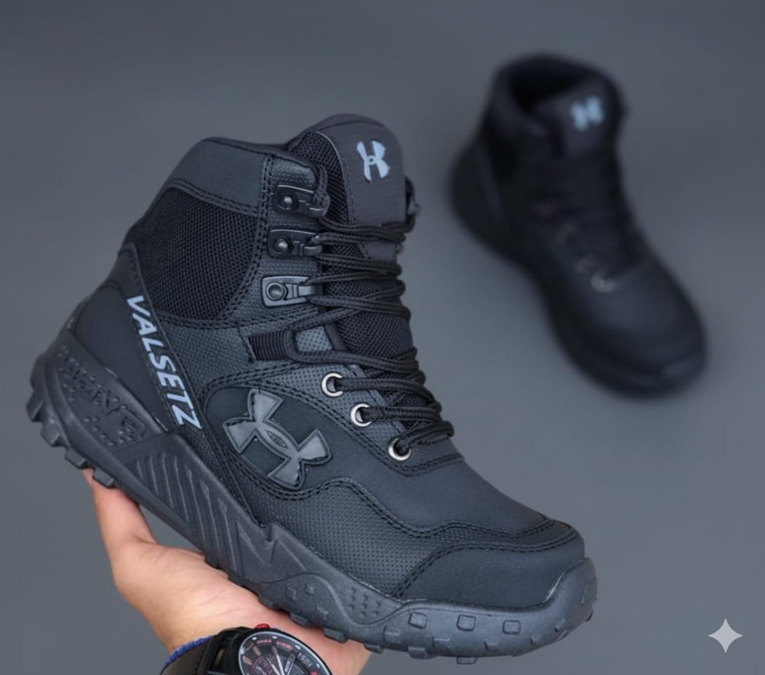 Una mano sosteniendo una bota táctica Armour™ negra, mostrando en detalle los materiales de alta calidad y las costuras reforzadas.