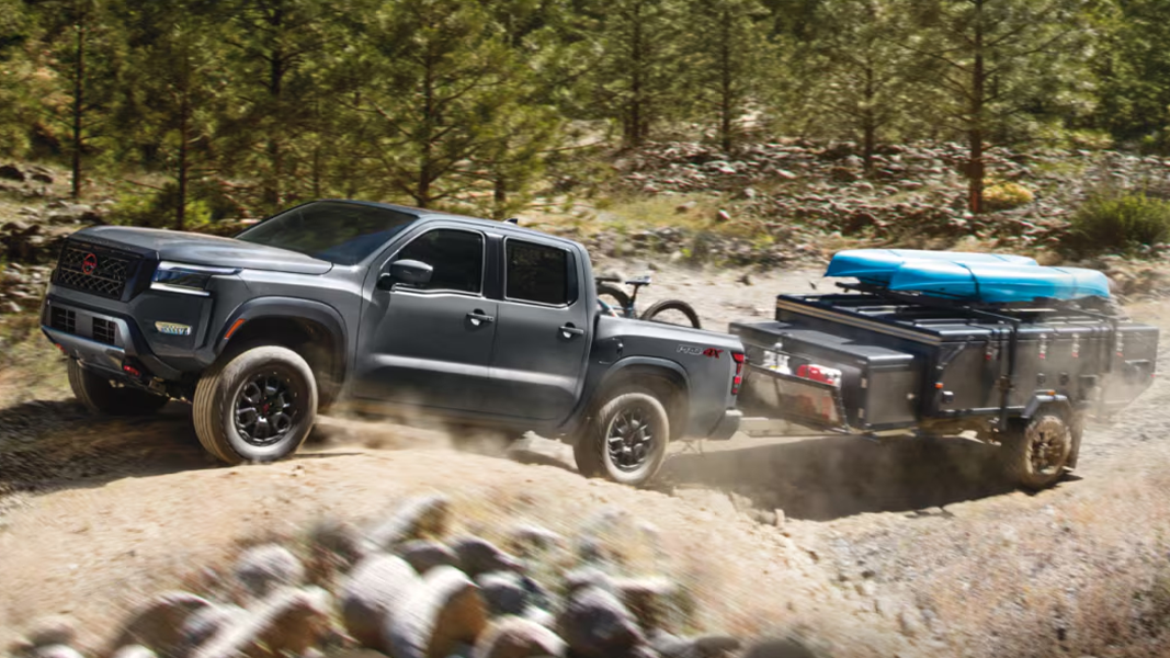 Vue 3/4 avant et latérale du Nissan Frontier 2025 sur route de sable escarpé tractant une remorque avec kayak
