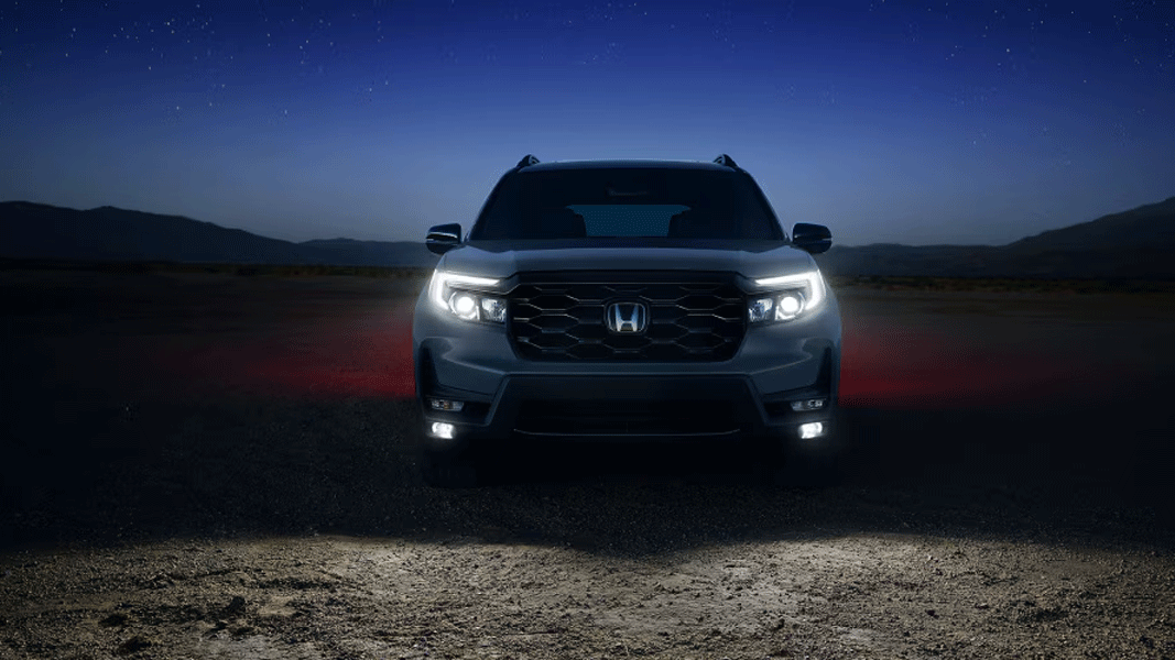 Vue avant du Honda Passport 2025 avec les phares allumées, sur route de sable en pleine nuit avec ciel étoilé