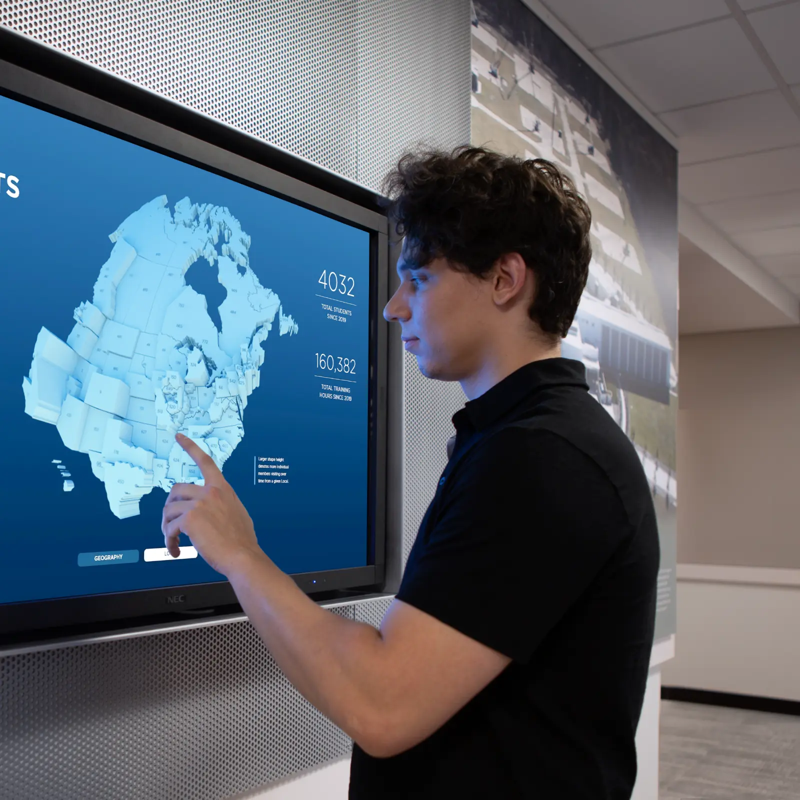 Man interacts with Students at ITEC United States map data visualization on wall-mounted touchscreen display