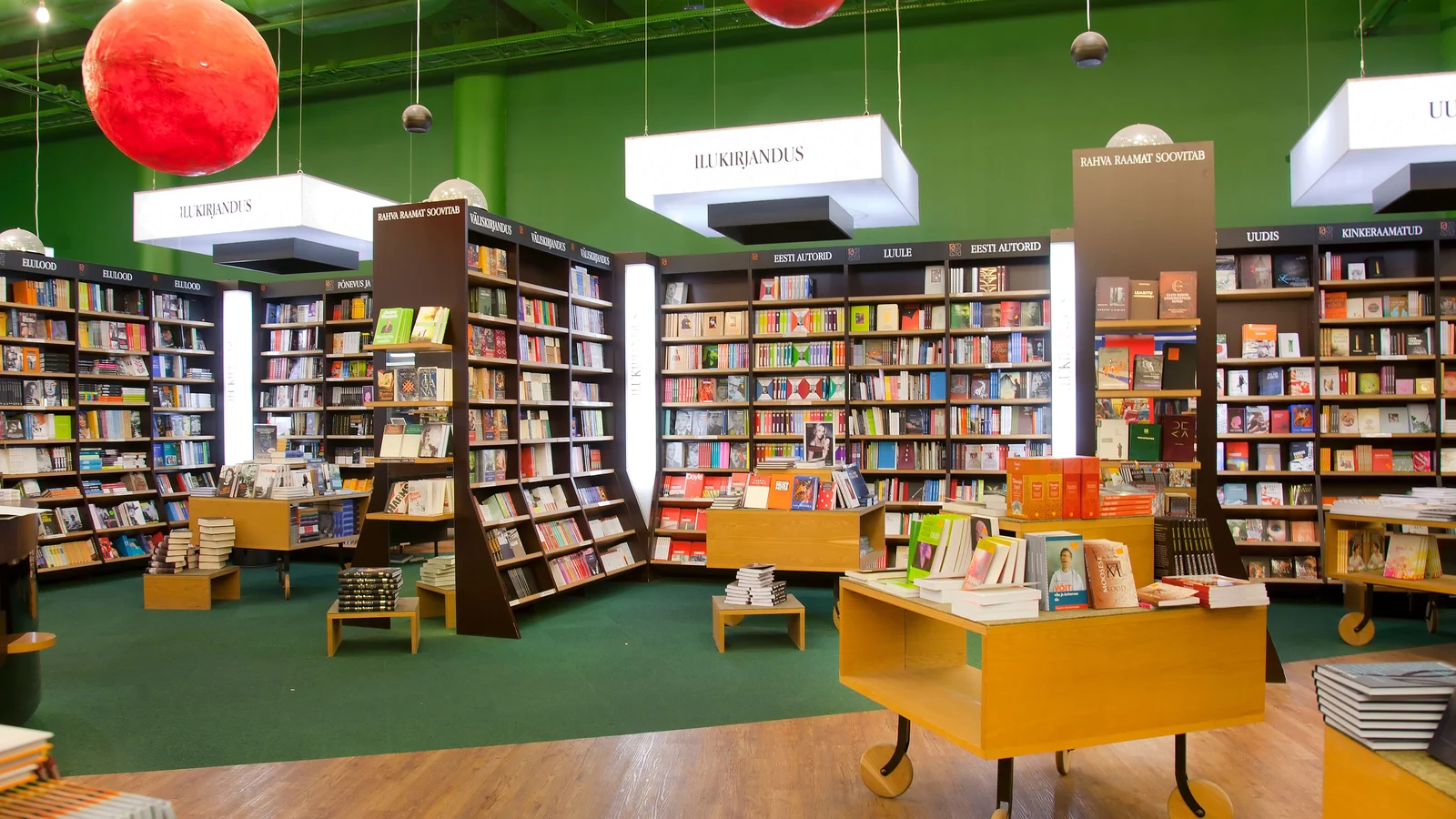 Buchhandlung mit Bücherregalen, Auslagetischen und grünen Wänden.