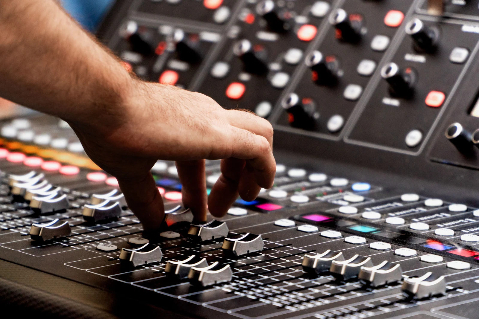 Eine Hand bedient die Schieberegler eines Audiomischpults.