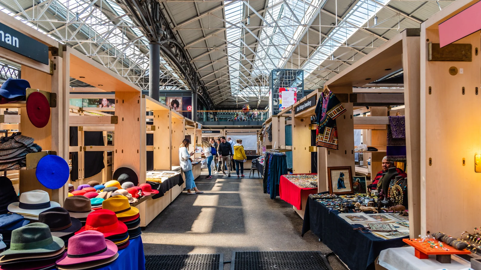 Besucherinnen und Besucher zwischen Verkaufsständen in einer hellen Markthalle.