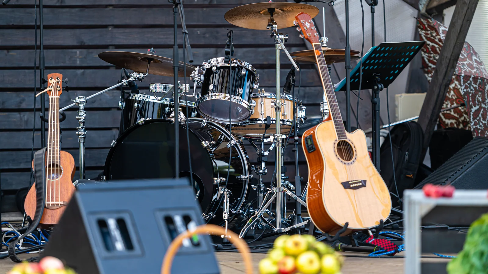 Gitarre, Ukulele und Schlagzeug stehen zwischen Mikrofonen und Monitorboxen auf einer Bühne.
