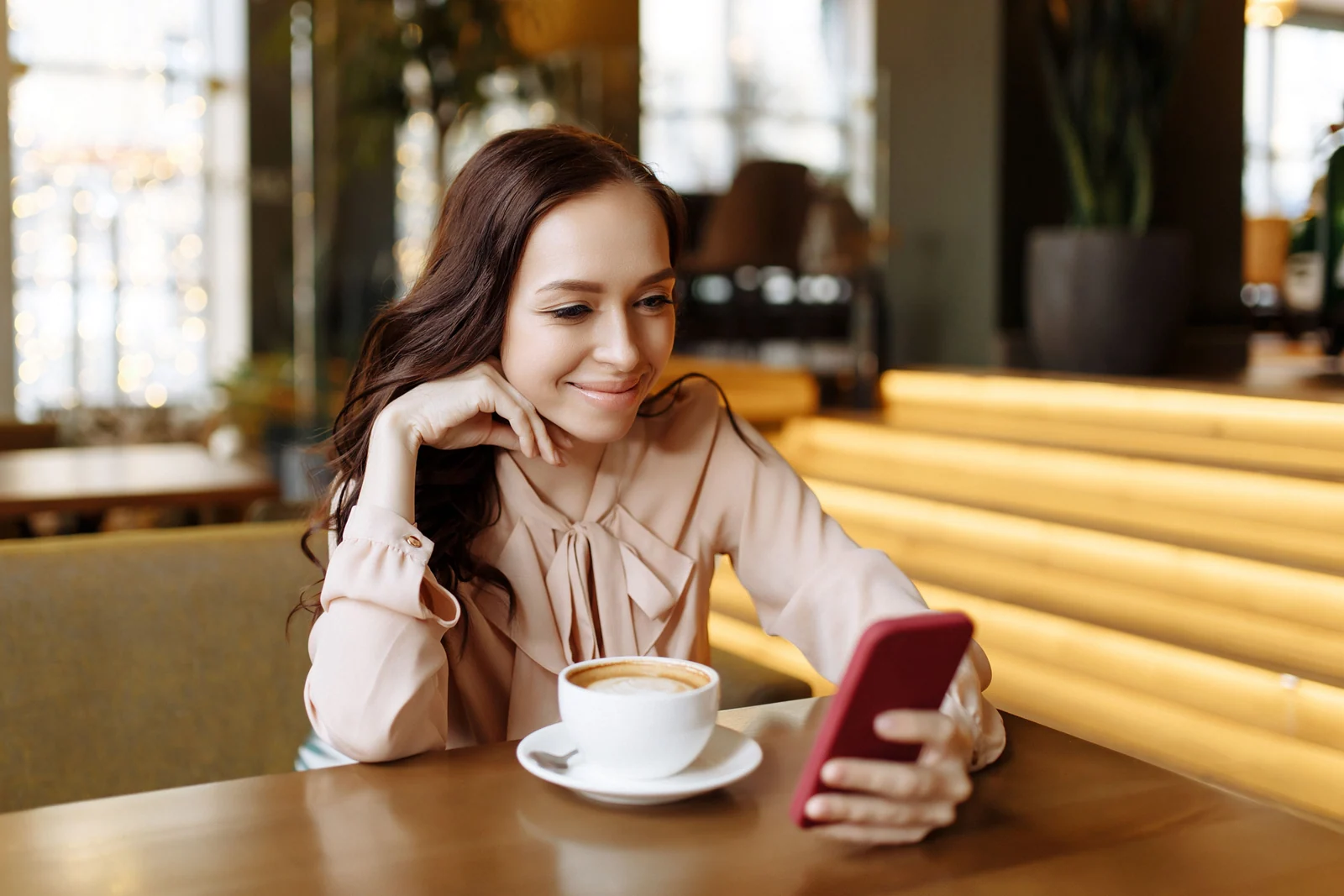 Frau betrachtet ein rotes Smartphone an einem Cafétisch mit einer Kaffeetasse