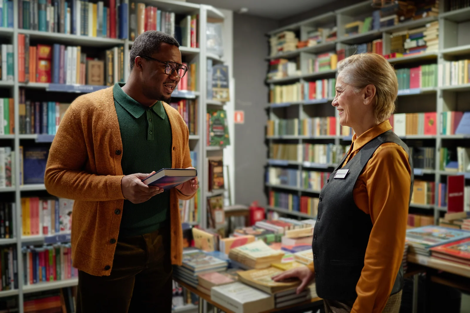 Zwei Menschen sprechen vor gefüllten Bücherregalen über ein Buch.