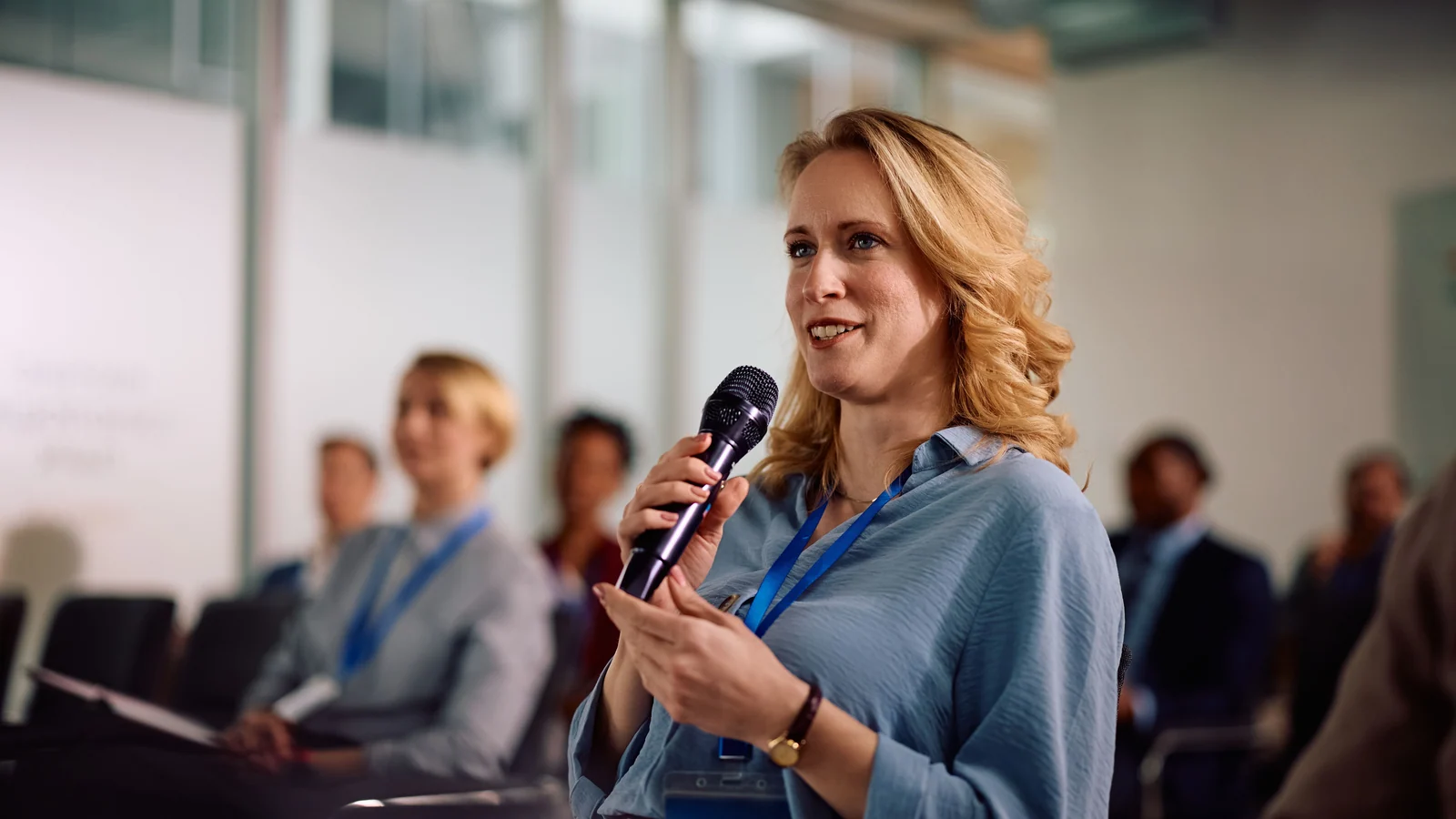 Frau mit Mikrofon zwischen Teilnehmenden eines Seminars