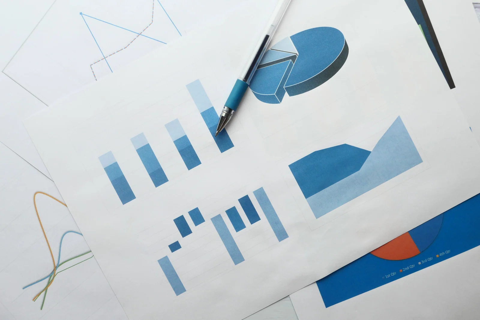 Ein blauer Stift liegt auf ausgedruckten Balken-, Kreis- und Liniendiagrammen.