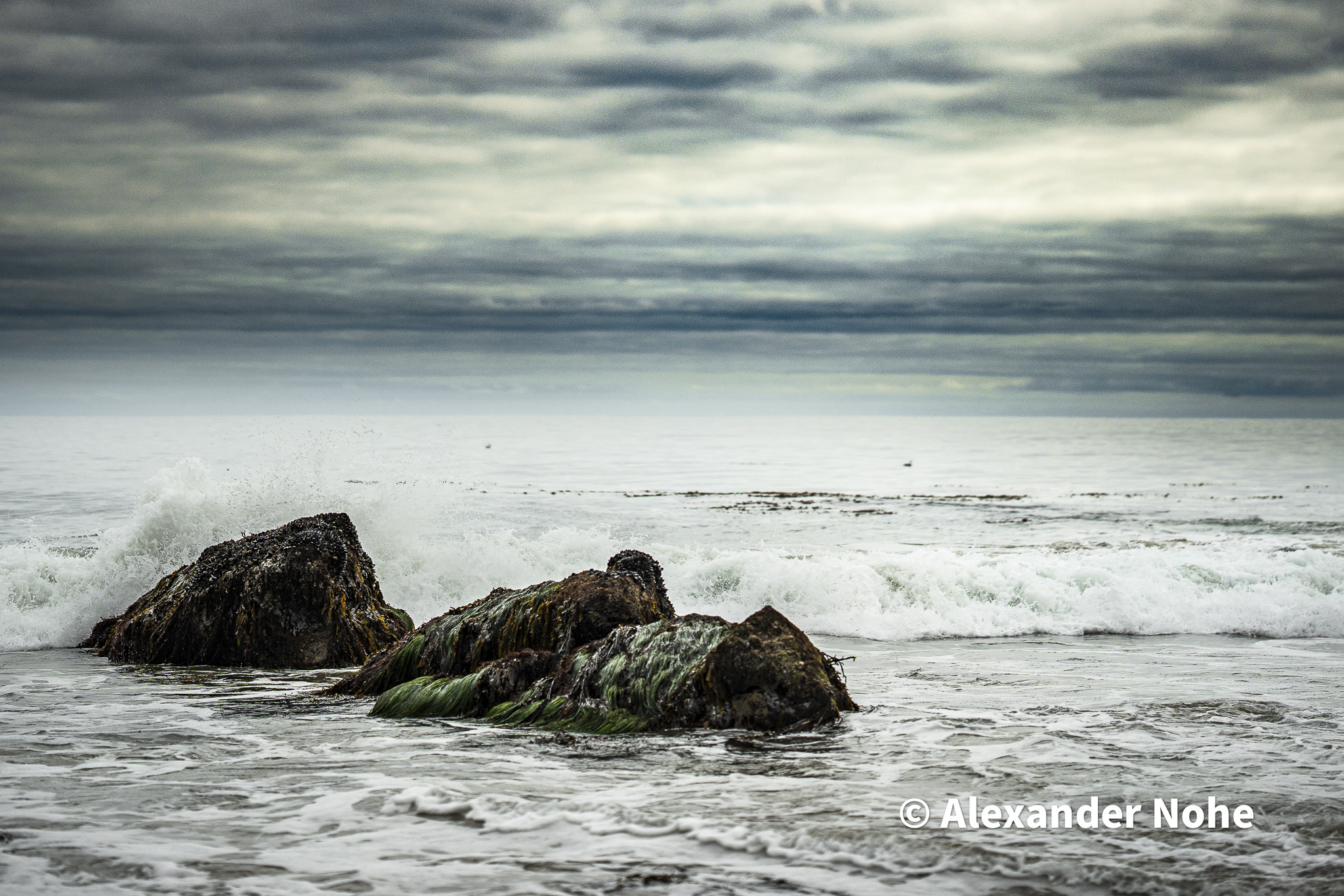 Mossy green rocks with ocean waves crashing against them