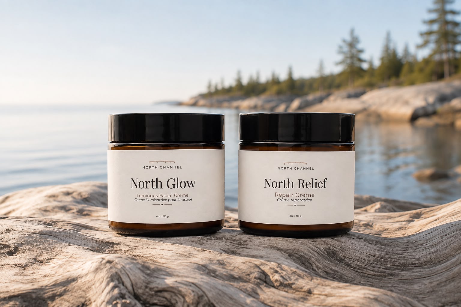 North Glow and North Relief crèmes standing together on weathered driftwood, still water and a pine shoreline behind them