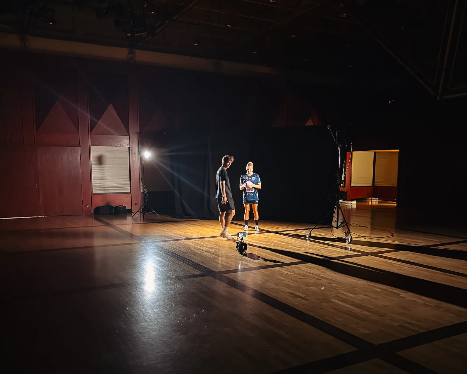 Zwei Spielerinnen im Scheinwerferlicht auf dem leeren Hallenboden, daneben Licht auf Stativen