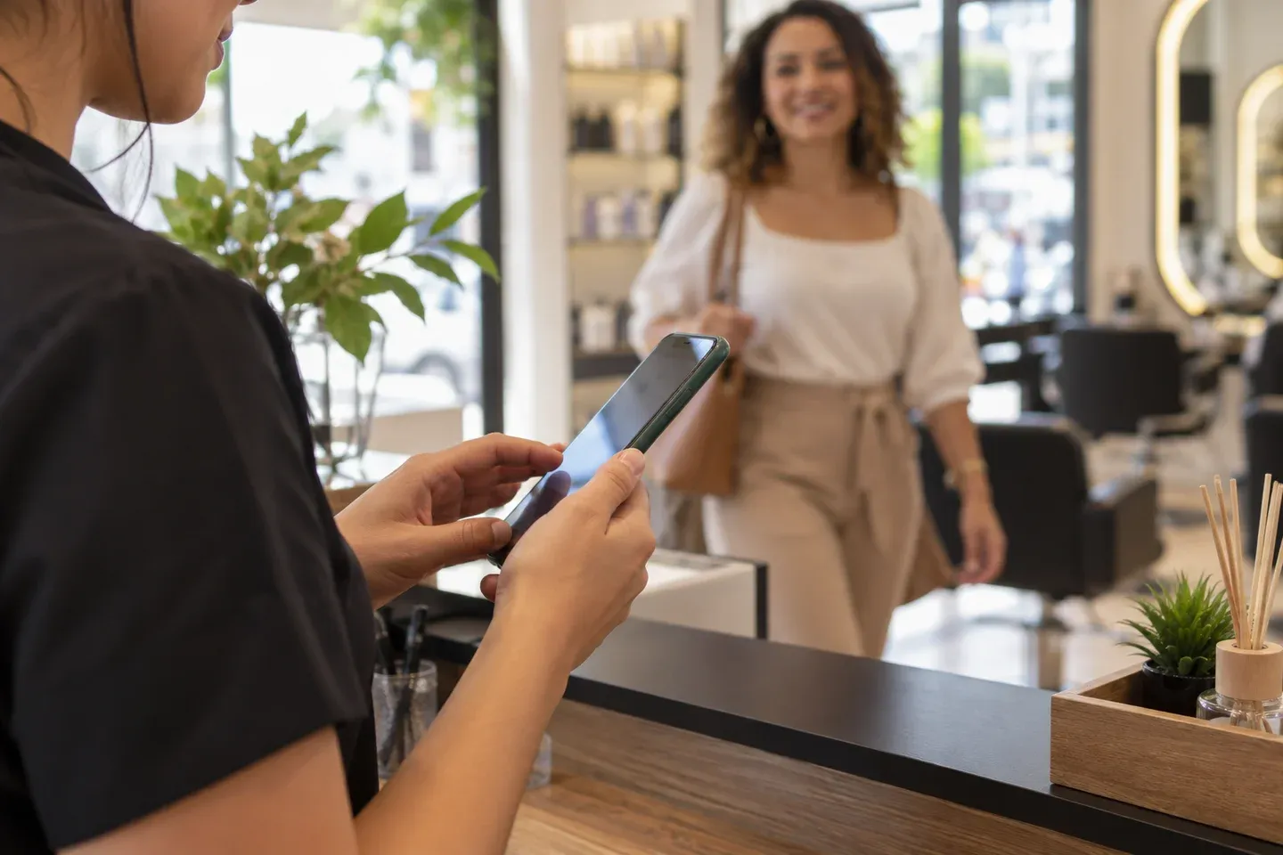 Recepcionista usando o celular enquanto uma cliente chega ao salão