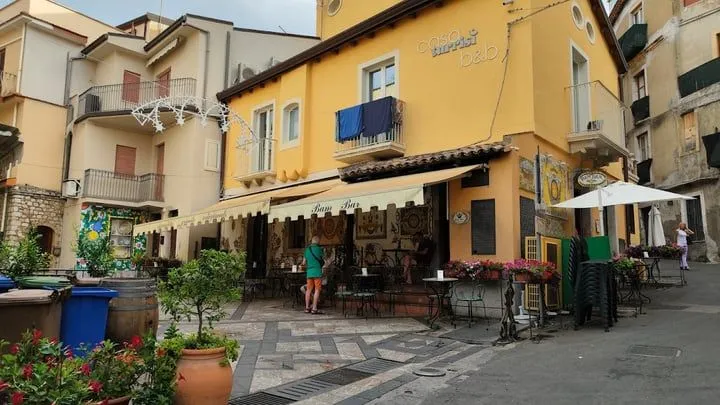 The image is well-composed, capturing a vibrant street scene with a yellow building and a bar. Key elements are in focus, and the photo is realistic with accurate colors. The main weakness is the flat lighting, which makes the scene appear somewhat dull, lacking dynamic range and strong highlights.