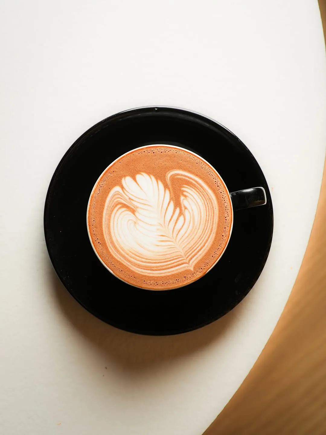 An expertly composed and well-lit image of a latte with intricate latte art. The image is sharp, color-accurate, and highly photo-realistic, with the key element (the latte art) in perfect focus. The overall aesthetic is clean and professional.