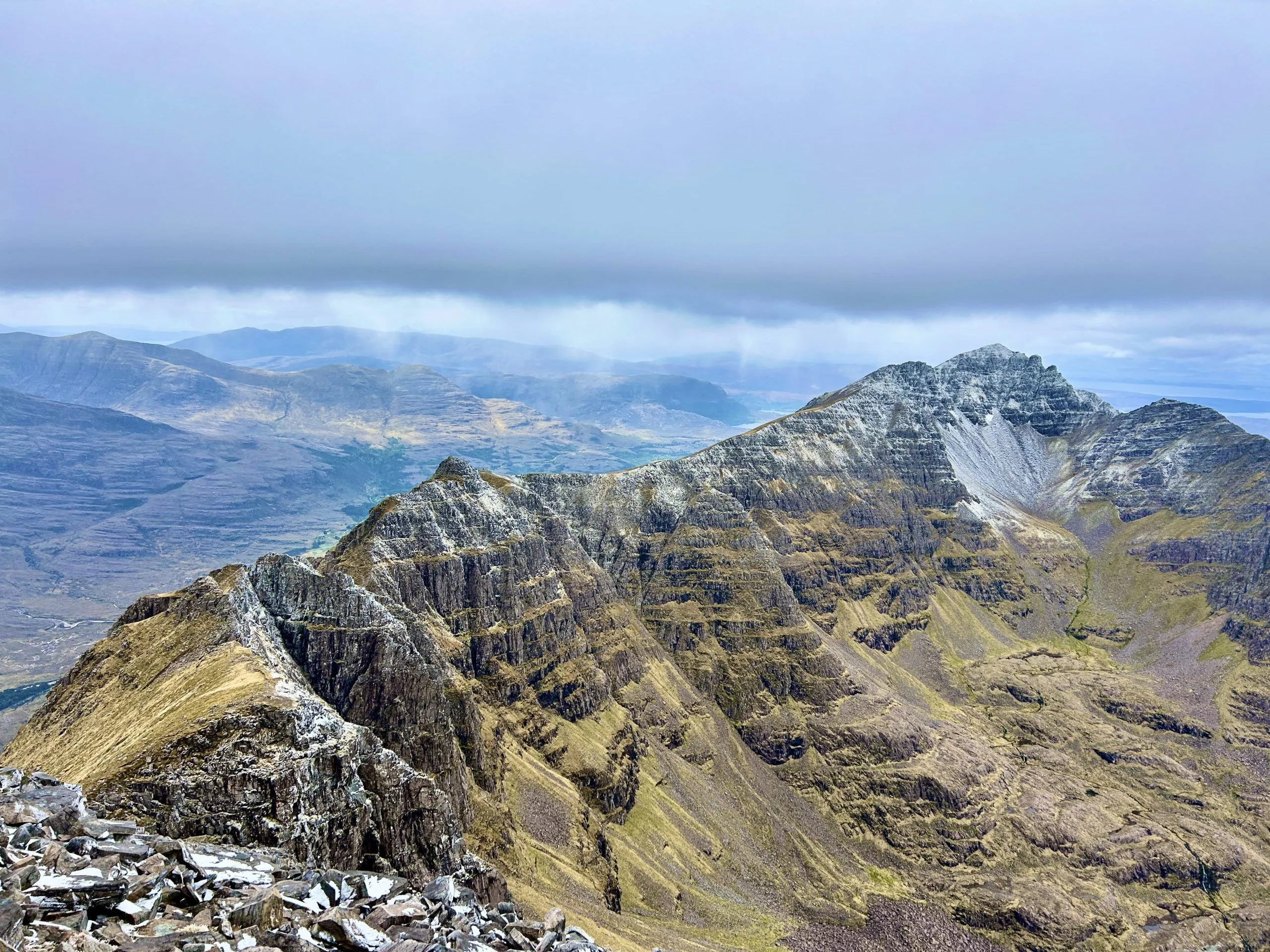 An aerial view of a rugged mountain range under a cloudy sky, showcasing the natural textures of the peaks and valleys.