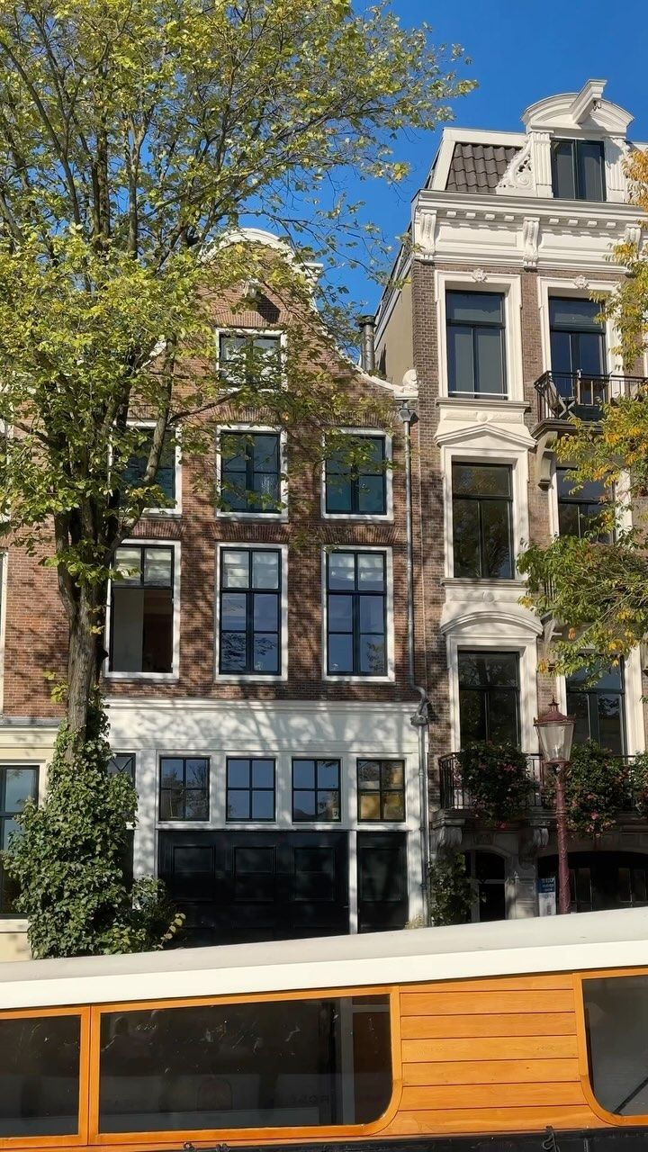 This image showcases well-composed exterior photography of Amsterdam canal houses. The composition is pleasing, with the trees framing the buildings nicely. Lighting is excellent, with natural sunlight illuminating the scene. The image is sharp, with good detail visible in the brickwork and window frames. Color accuracy is high, representing the warm tones of the brick and the green of the trees accurately. The photo is photorealistic and all key elements (buildings) are in focus. No unwanted elements are present. 

Score Breakdown (out of 100):
Well-composed: 21/25
Well-lit: 15/15
Sharp: 20/20
Color-accurate: 10/10
Photo-realistic: 20/20
Key elements in focus: 10/10