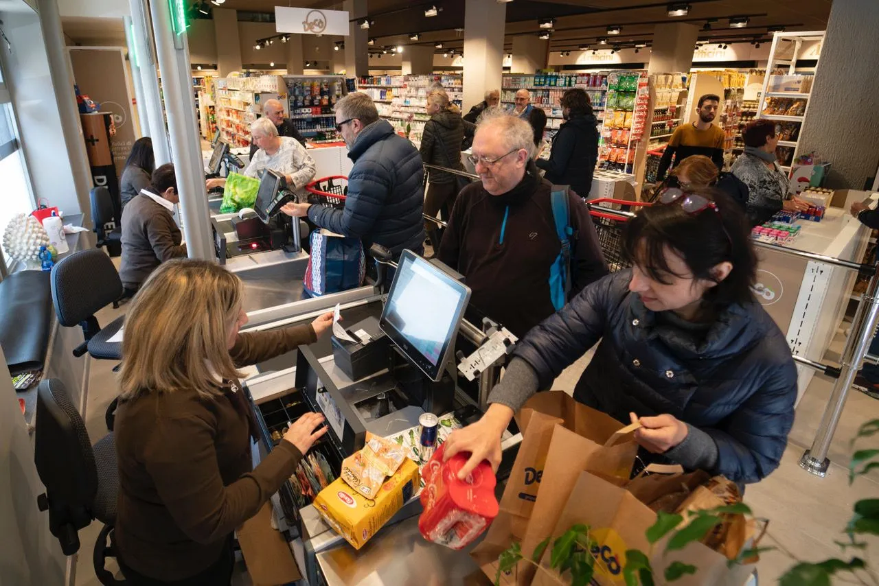 A candid scene at a busy grocery store checkout, showing customers and a cashier processing items.