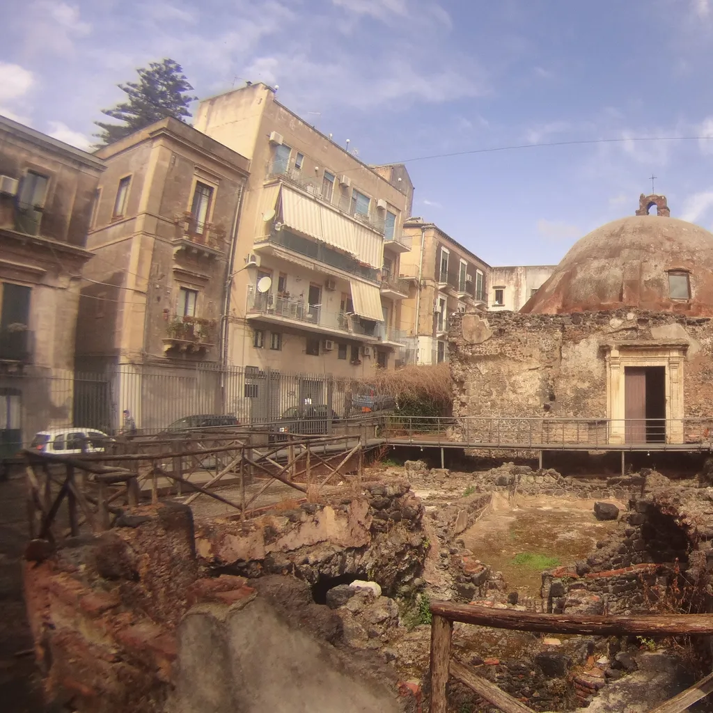 The image captures an ancient domed structure amidst archaeological ruins, framed by surrounding city buildings and modern walkways.