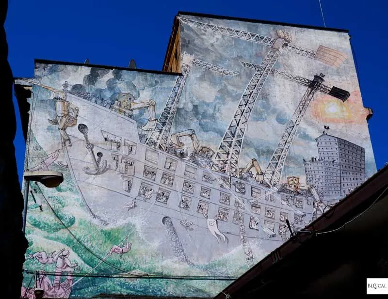 The image is a well-exposed and sharp photograph of a large, detailed mural on the side of a building. The lighting is excellent, illuminating the artwork evenly, and the key elements of the mural are in clear focus. The colors appear accurate and natural for a building mural, and the photograph itself is highly photo-realistic. The primary weakness lies in the composition, which includes some distracting dark elements in the bottom right foreground that partially obscure the mural and could be cropped out for a stronger focus on the artwork.
