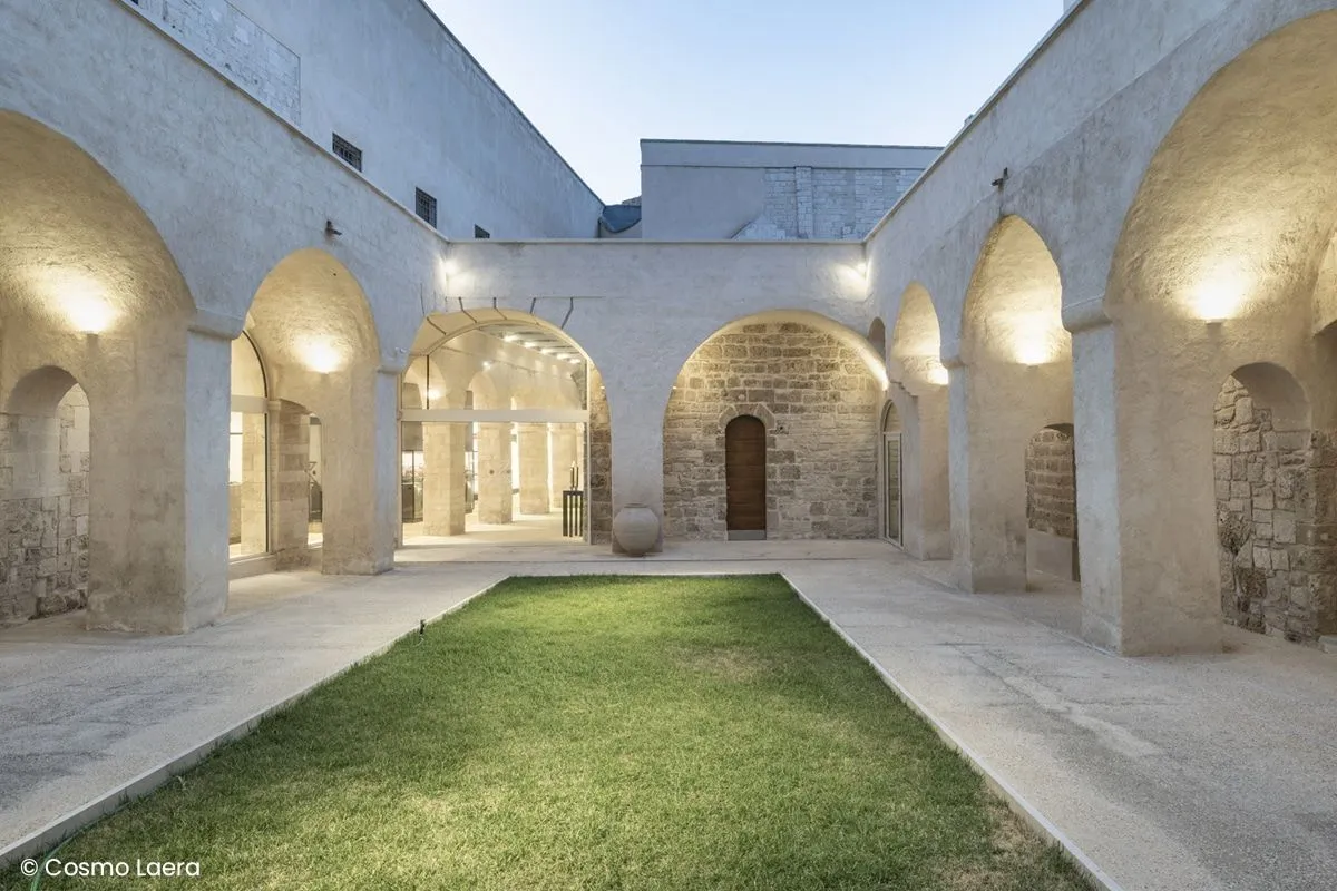 A well-composed and well-lit architectural shot of a minimalist courtyard featuring stone arches and a central patch of vibrant green grass. The image is sharp, color-accurate, and highly photo-realistic, with all key elements in focus. The lighting beautifully highlights the textures of the stone and the depth of the space.
