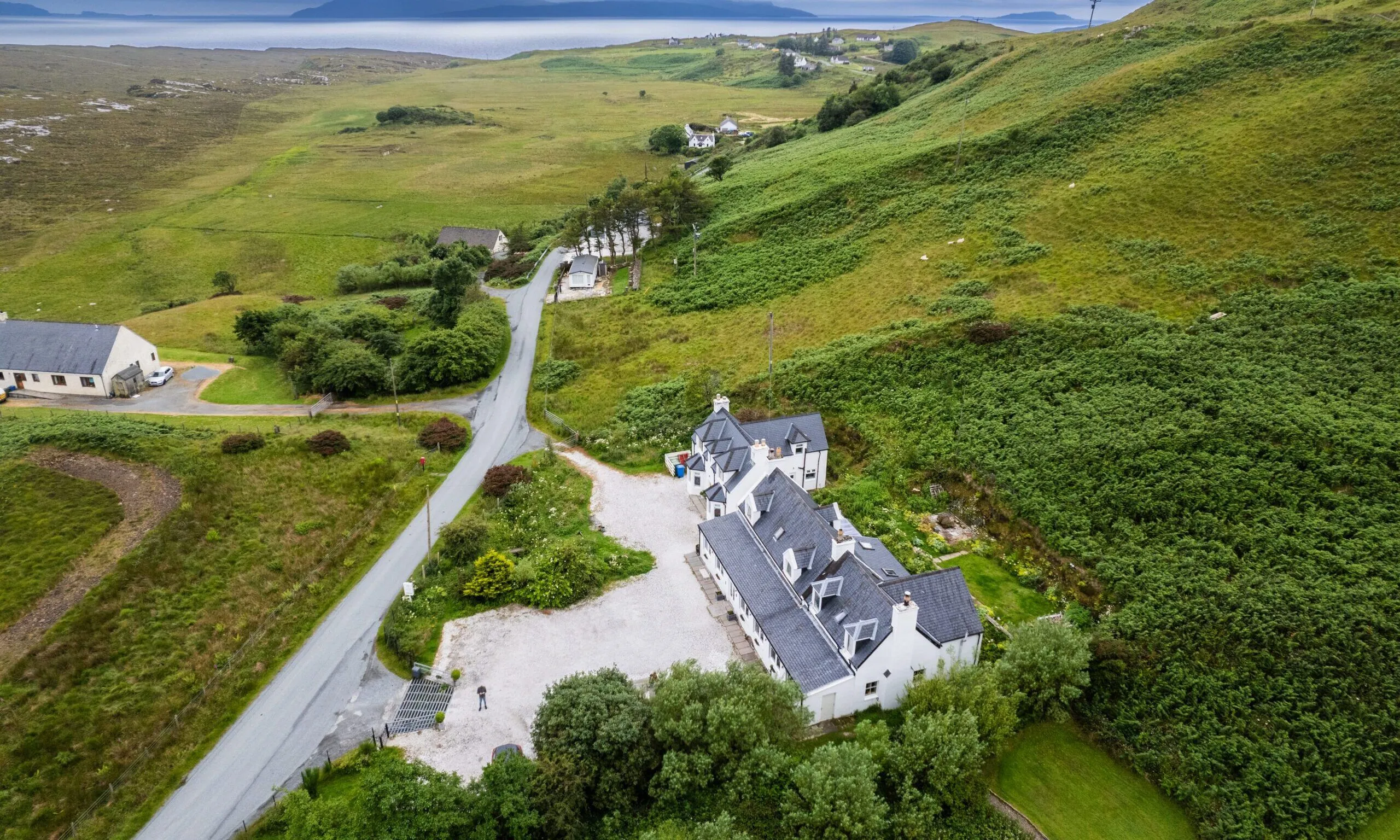 The image showcases a well-composed aerial view of a white building complex nestled in a vibrant green landscape. It features excellent sharpness and realistic depiction with natural, even lighting. All key elements are clearly in focus.