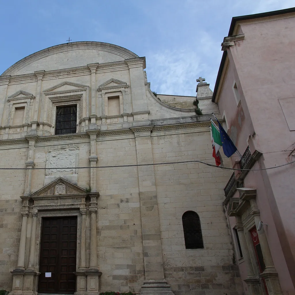 A front view of a historic stone church building with a large wooden door, two bell towers, and intricate facade details under a blue sky.