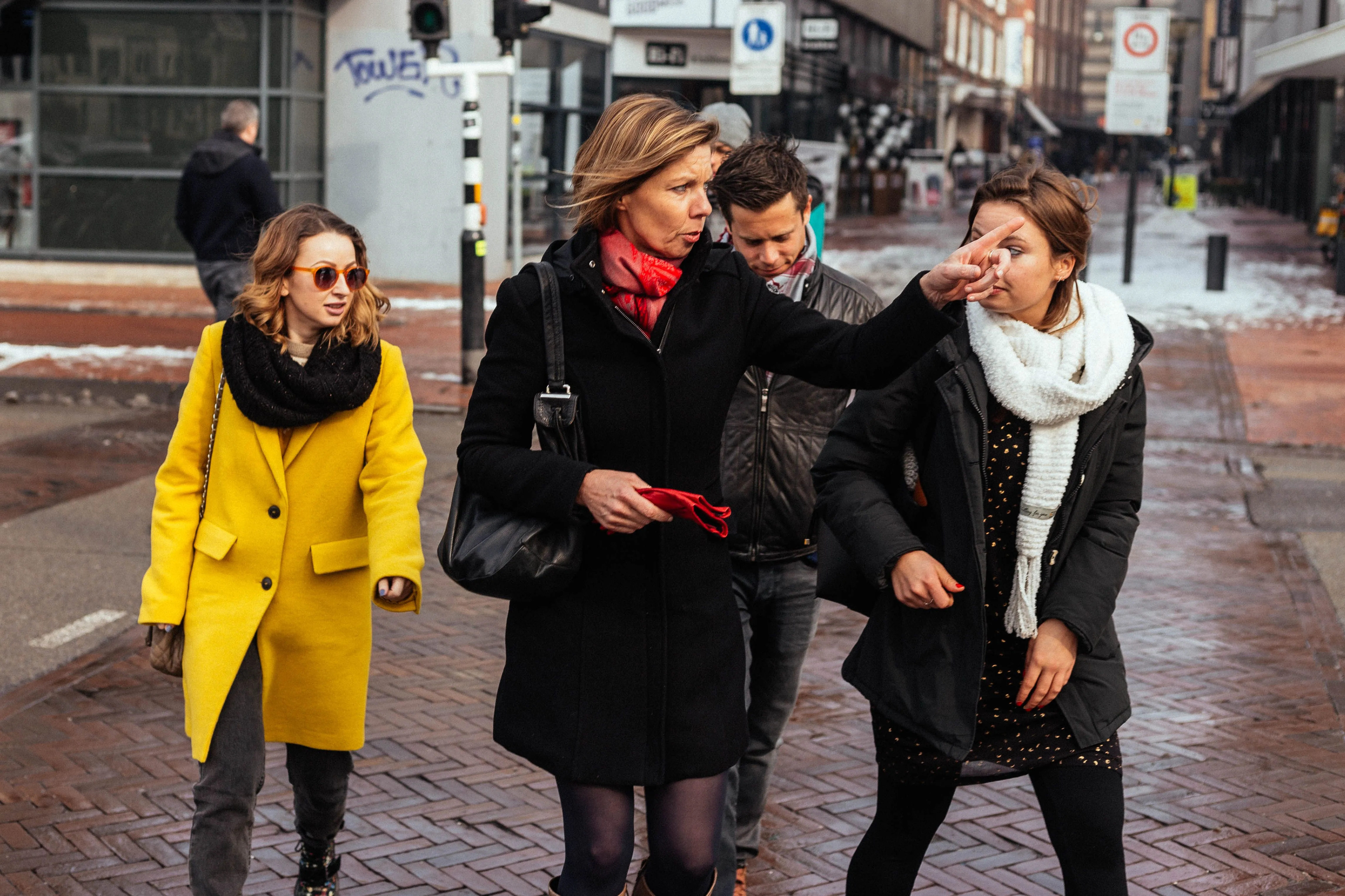 This candid street photograph features a group of people interacting in an urban setting. The image is sharp with good focus on the key subjects and displays natural, accurate colors. The composition is effective in capturing the moment, though the lighting is a bit flat, contributing to a slightly subdued overall impression.