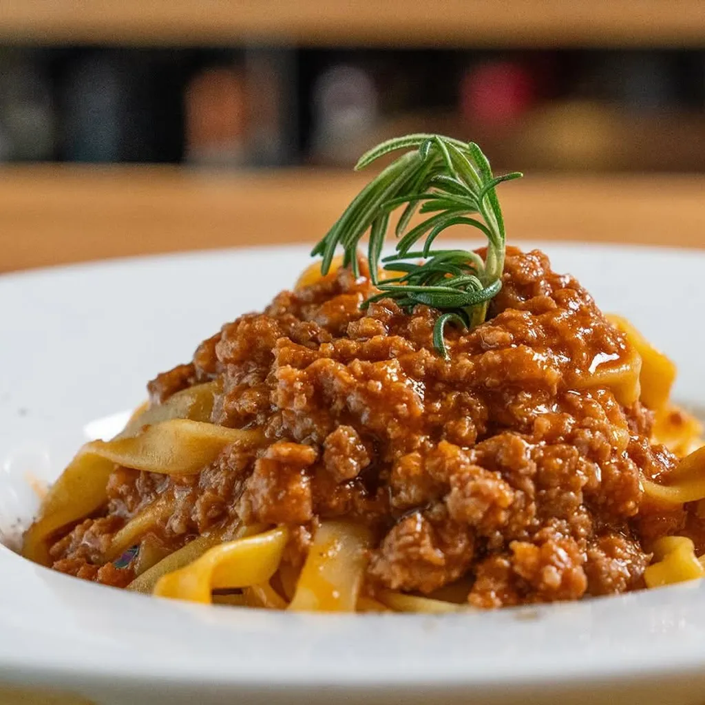 A well-composed and appetizing close-up of pasta with bolognese sauce, garnished with rosemary. The image is well-lit, sharp, and highly photo-realistic, showcasing the dish's texture and color accurately.