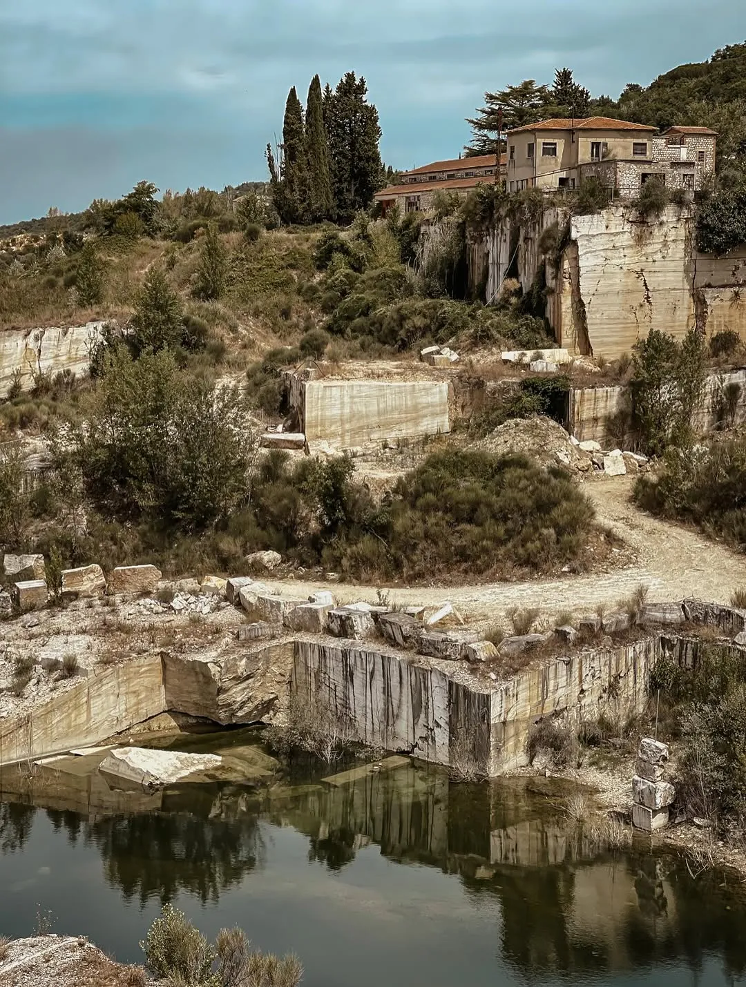 The image displays a well-composed view of a quarry with a reflective body of water in the foreground and buildings nestled on a hill in the background. The key elements are in focus, contributing to its photo-realistic quality.