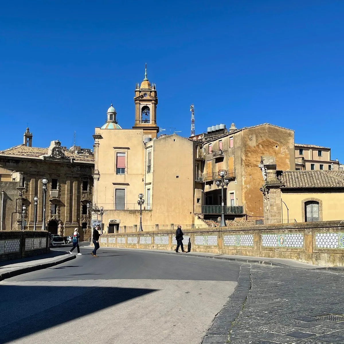 A vibrant street scene showcasing historic architecture, a bridge, and pedestrians under a clear blue sky.