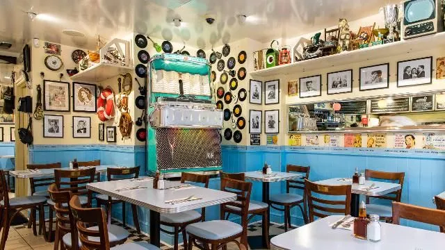 This image effectively captures the vibrant and retro interior of a diner, featuring a prominent jukebox and themed decor. The lighting is well-balanced, contributing to a pleasant atmosphere. The colors are accurate and lively, and the overall image is photo-realistic. While key elements like the jukebox are in focus and sharp, the composition could be slightly improved; some foreground tables are partially cut off, and the scene feels a little cramped, though the decor itself is part of the desired aesthetic and not considered clutter.