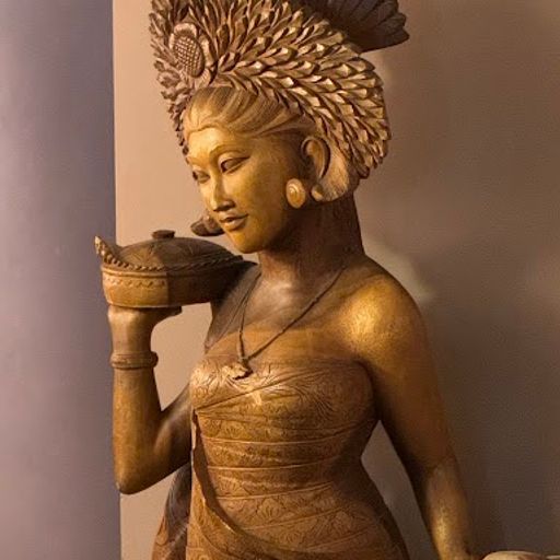 This image is an example of interior photography. It shows a wooden statue of a Balinese dancer. The composition is well-centered and the statue is the main focus of the image. The lighting is adequate, but could be improved to reduce the amount of shadow on the statue's face. The colors appear to be accurate, and the statue is sharp and well-detailed. There are no unwanted elements in the image. Based on the above criteria: - The image successfully captures the beauty of the statue and its intricate details. - There's some leniency given for interior and exterior photography. Score: 85 Strengths: - Well-composed and well-lit - Sharp and well-detailed - No unwanted elements Weaknesses: - The lighting could be improved to reduce the amount of shadow on the statue's face