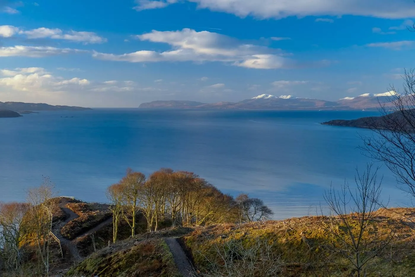 This image captures a breathtaking natural landscape with excellent composition, clarity, and color accuracy. The vast blue body of water and the distant snow-capped mountains create a serene and expansive view.