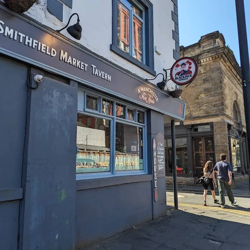The image captures the exterior of 'Smithfield Market Tavern' on a clear day. Strengths include good lighting, sharp detail on the building and signage, accurate colors, and a photo-realistic quality. The key elements, primarily the pub, are well in focus. The composition is generally good, although the slight tilt and the partial street pole on the right slightly detract from its perfection.
