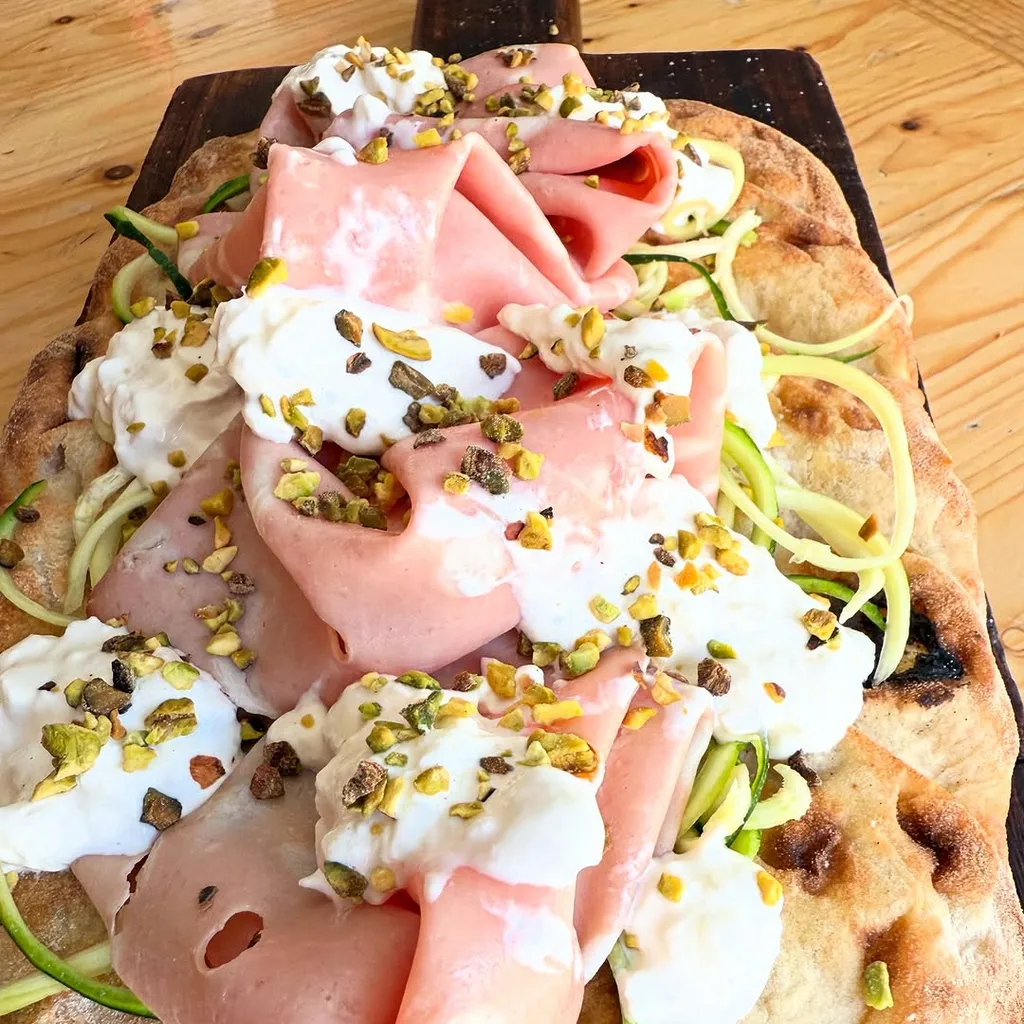 The image is sharp and features the key elements well in focus, particularly the mortadella, burrata, and pistachios. Colors appear accurate and the overall image is photo-realistic. The composition effectively frames the dish, making it the central subject. While generally well-lit, some areas, especially on the cheese, exhibit slightly harsh highlights, and the lighting could be more diffused to enhance texture and depth.