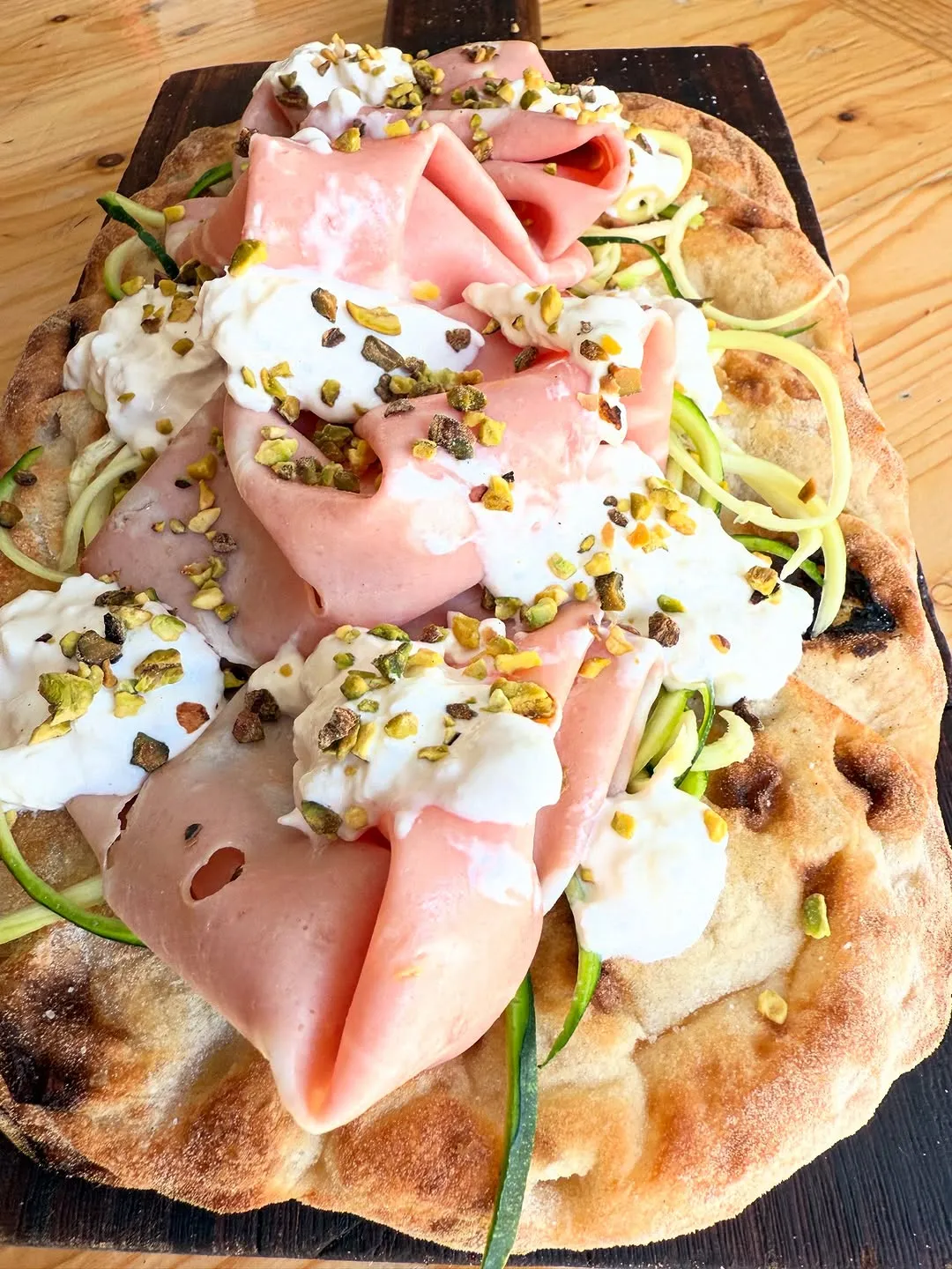 The image is sharp and features the key elements well in focus, particularly the mortadella, burrata, and pistachios. Colors appear accurate and the overall image is photo-realistic. The composition effectively frames the dish, making it the central subject. While generally well-lit, some areas, especially on the cheese, exhibit slightly harsh highlights, and the lighting could be more diffused to enhance texture and depth.