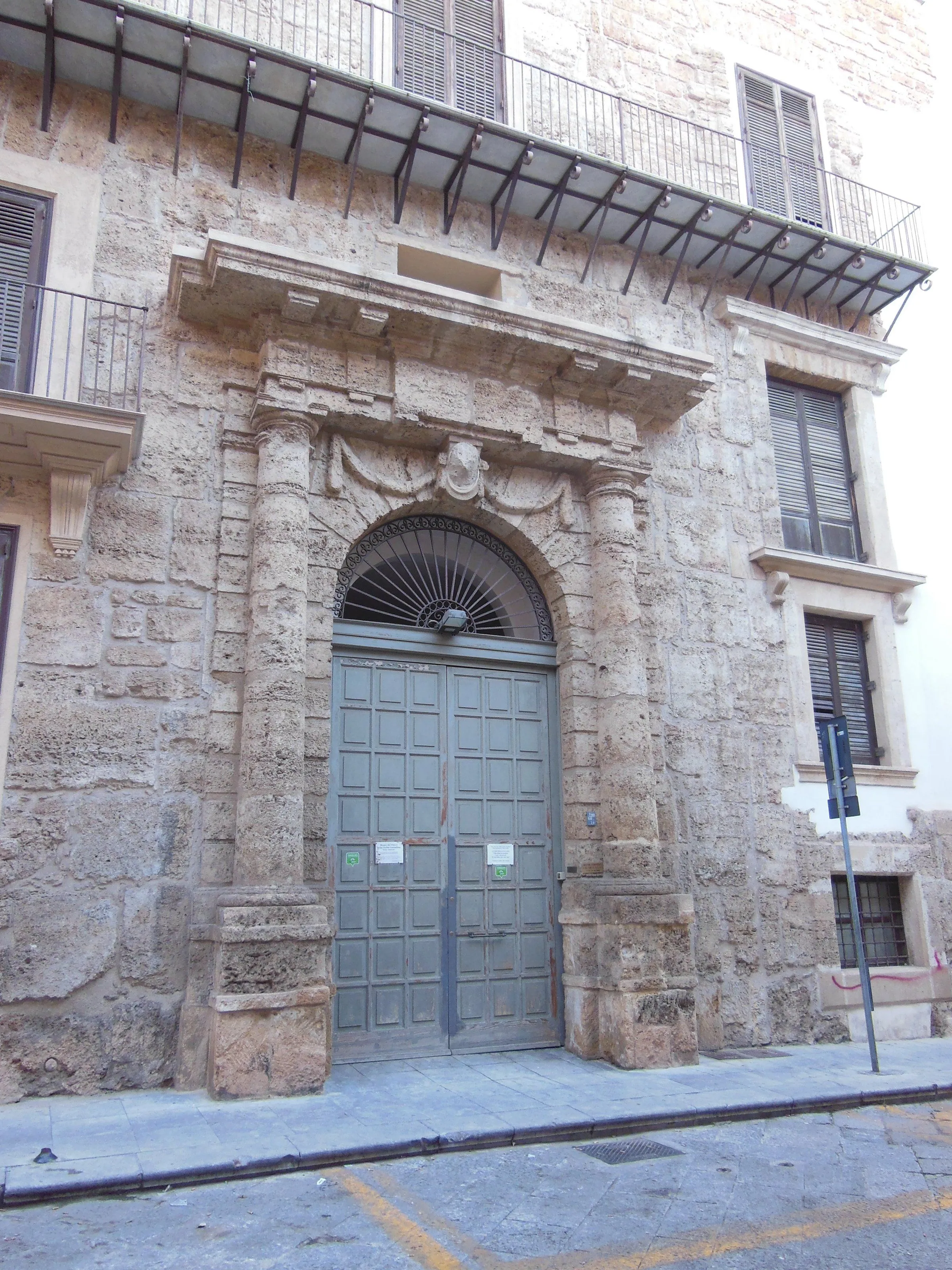 An editorial style image showcasing the ornate entrance of an old stone building. The image is focused on the large wooden door and the decorative stone archway above it.