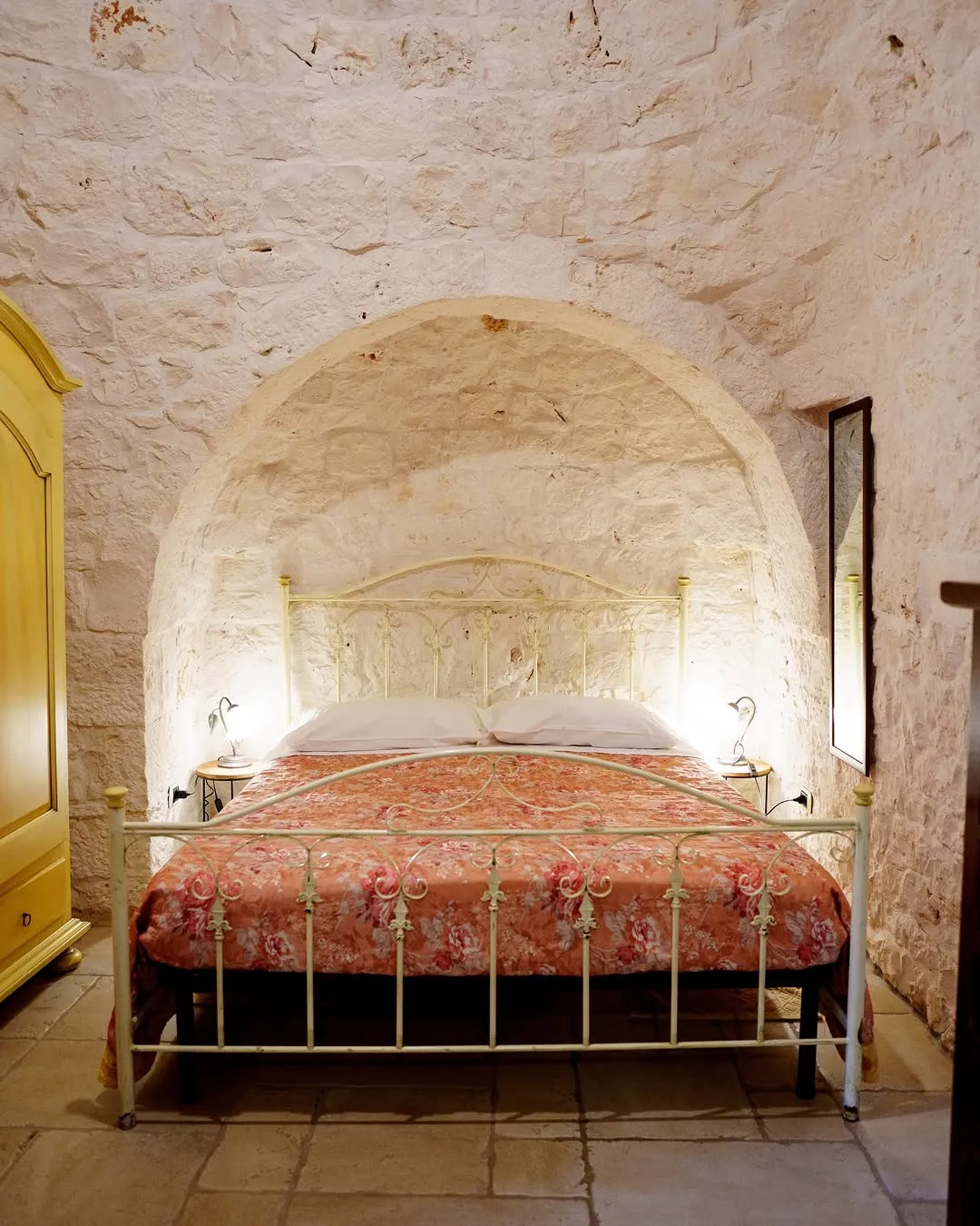 The image displays a well-composed and sharp photograph of a bedroom with unique architectural features, including an arched stone ceiling and walls. The lighting is balanced and highlights the textures of the room.