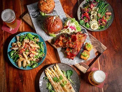 An overhead shot showcasing a diverse meal spread including burgers, ribs, various salads, and asparagus on a rustic wooden table. The composition highlights the individual dishes, presenting a vibrant and appealing dining scene.