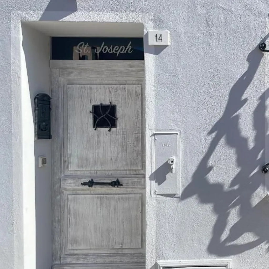 An editorial style image showcasing architectural details of a building exterior with a door, window, and an ornate metal grate, accentuated by strong sunlight and dramatic shadows.