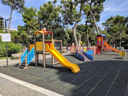 A bright, well-lit photograph of a colorful children's playground under a clear sky. The main playground structures are sharp and in focus, showcasing vibrant colors.