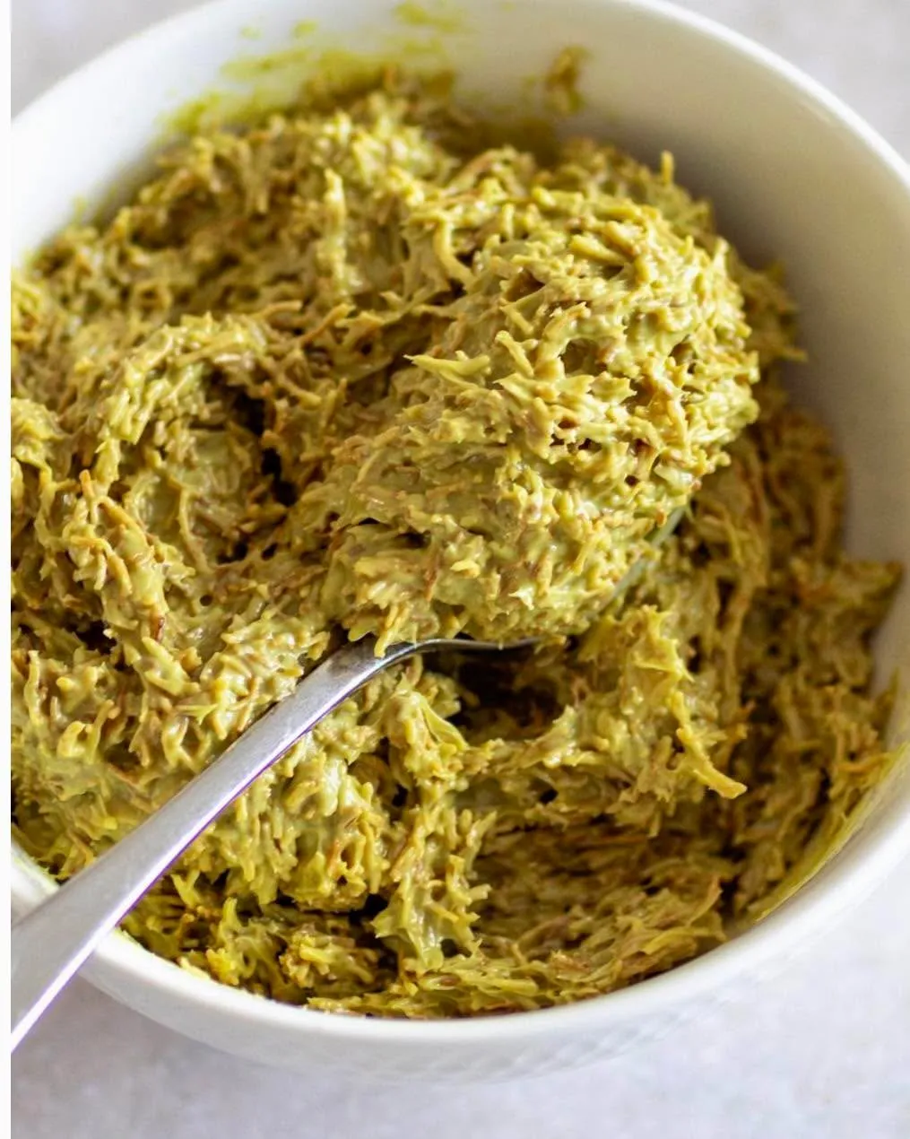 A well-composed and sharp close-up image of a green, textured food item in a white bowl, with a spoon partially submerged. The lighting is even, highlighting the food's intricate texture, and the colors appear natural and accurate.