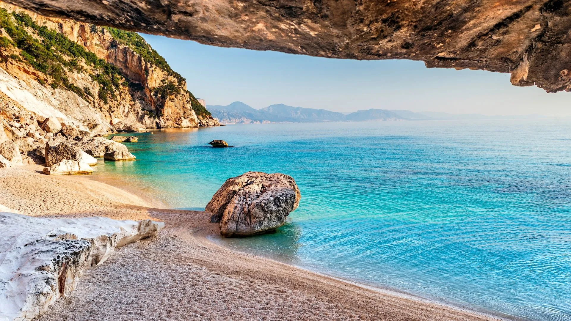 This image perfectly encapsulates an editorial style. The composition is strong, utilizing the cave opening as a natural frame for the stunning beach and clear turquoise water. The lighting is excellent, showcasing vibrant and accurate colors, and the image is sharp throughout, with all key elements in focus. The photo-realistic quality is very high.