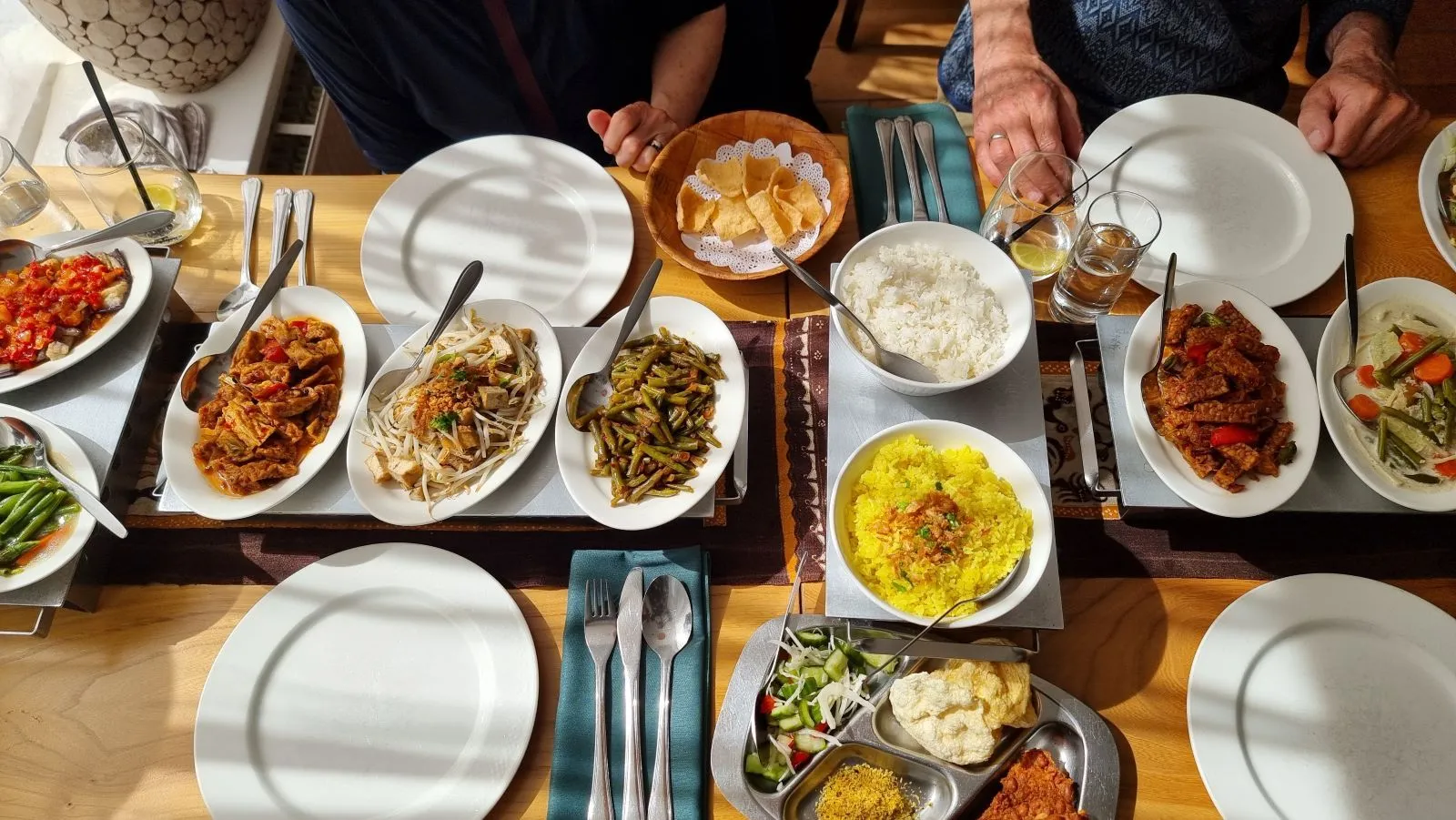 An overhead shot of a table set with a variety of vibrant dishes, including rice, green beans, and other accompaniments, suggesting a shared meal. The scene captures a warm and inviting dining experience.
