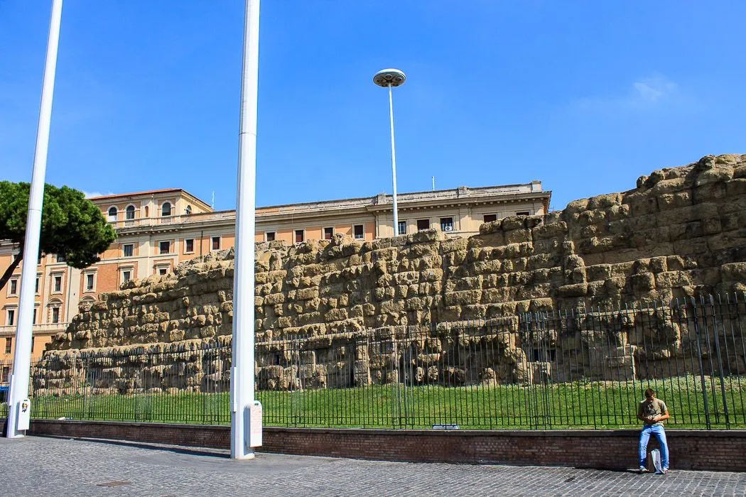 The image is generally of good technical quality, with appropriate lighting, sharpness, and color accuracy, and it is clearly photo-realistic. The historical stone wall and the building behind it are in good focus. However, the composition is significantly hampered by the prominent white pole in the foreground, which obstructs a large portion of the scene, particularly the historical wall, diminishing the overall visual appeal and balance of the shot.