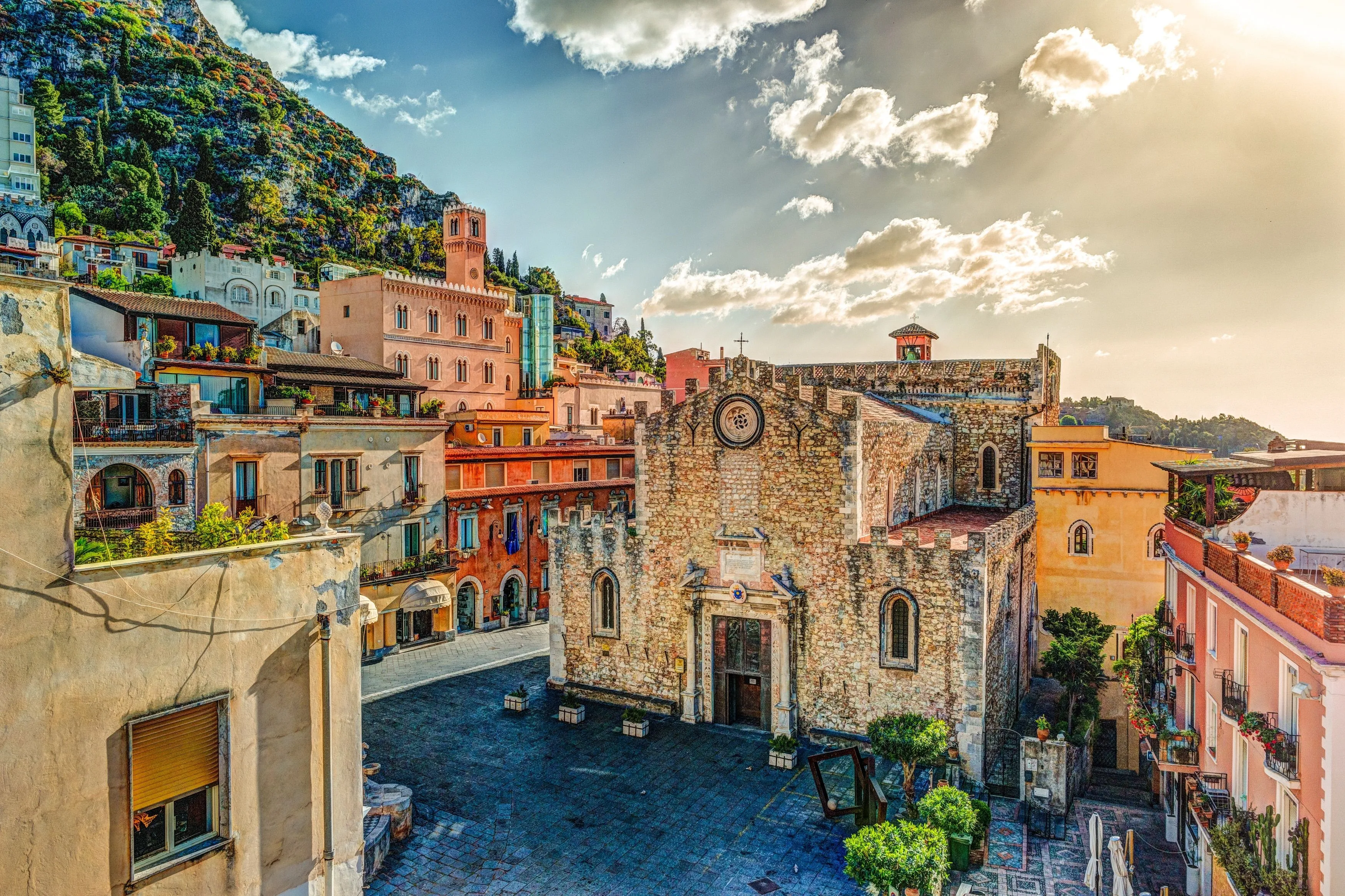 A vibrant and detailed photograph of a historic European town square, featuring an old stone church and colorful buildings under a bright, partly cloudy sky.
