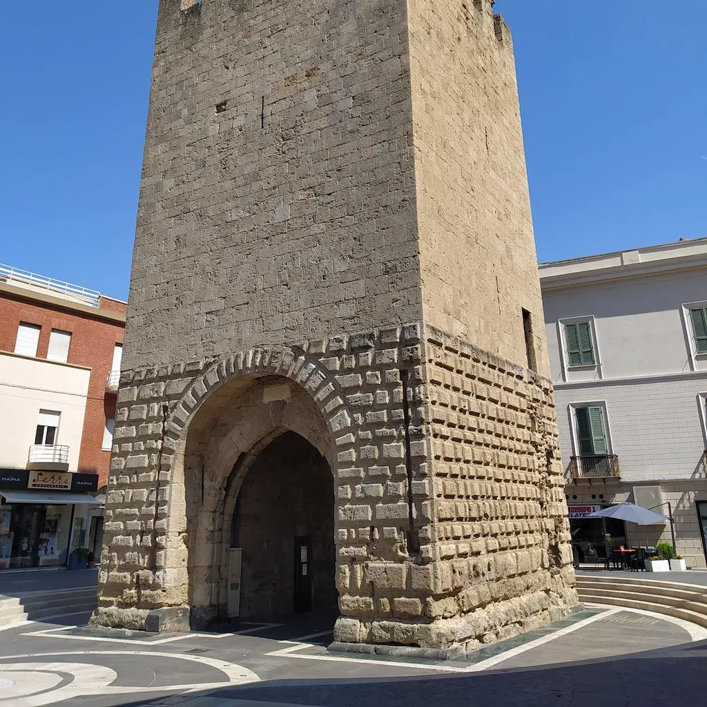 A well-lit and sharp photograph of an old stone tower with an archway, set against a clear blue sky. The image captures the historical details of the structure and appears highly photo-realistic.